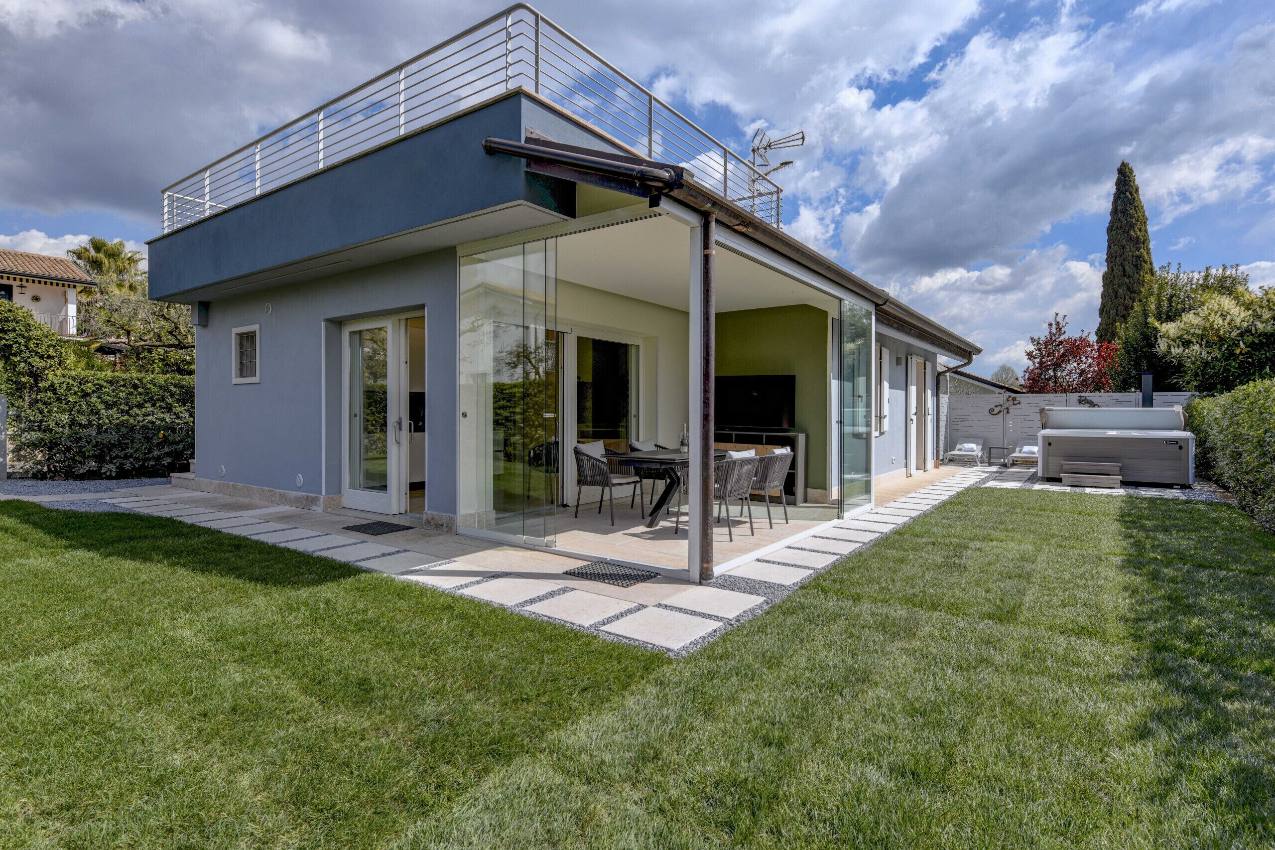 Ein modernes Haus mit überdachter Terrasse, großen Fenstern und einem gepflegten Rasen.