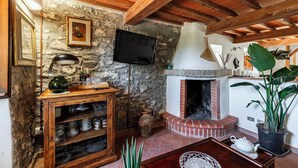 A rustic interior with exposed stone walls, a brick fireplace, wooden beams, a television, and a wooden cabinet with dishes. - Borgo Antico (Barberino di Mugello)