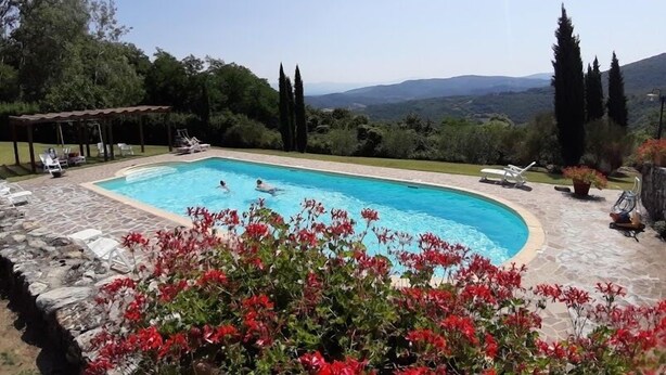 A swimming pool with a stone deck, surrounded by red flowers and greenery, with a view of distant hills. - Borgo Antico (Barberino di Mugello)