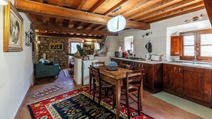 A rustic kitchen with wooden beams, a dining area with a table and chairs, and a stone wall with artwork. - Borgo Antico (Barberino di Mugello)