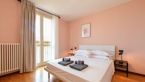 Un dormitorio con cama, mesitas de noche, un radiador, una ventana con cortinas y un cuadro colgado en la pared.