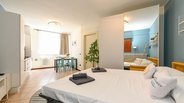 Ein Hotelzimmer mit einem Bett, einem Schreibtisch, einem Stuhl, einer Heizung, einer Pflanze und einem Fenster.