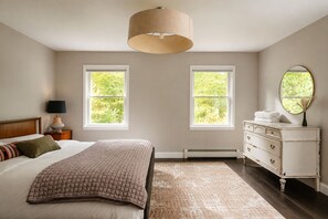 A bedroom with a bed, bedside lamp, dresser, mirror, and two windows. - Hot Tub, Fire Pit, Theater, Games & EV | Sleeps 8 (Barryville)