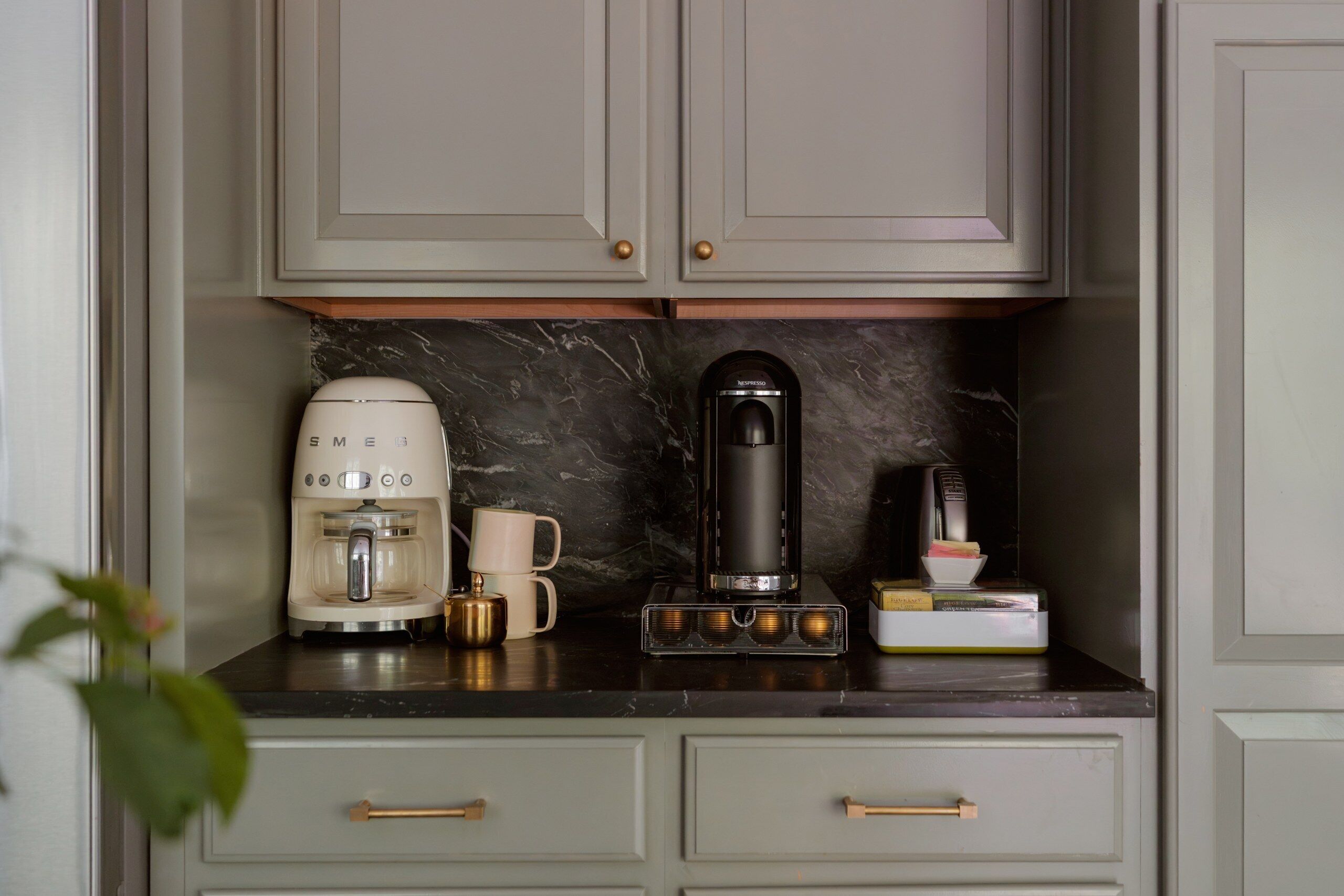 A kitchen with a coffee maker, a coffee machine, a mug, and a book on the counter.
