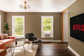 Una sala de estar con un sofá, una silla, una mesa de centro y una pantalla de televisión mostrando 'NETFLIX'.