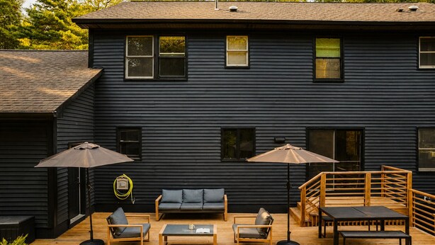 A dark wooden deck with outdoor furniture, including a sofa, chairs, and a table, and a staircase leading to an upper level.