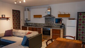 A compact kitchen with a stove, oven, and microwave. There is a wooden dining table and a sofa with cushions.