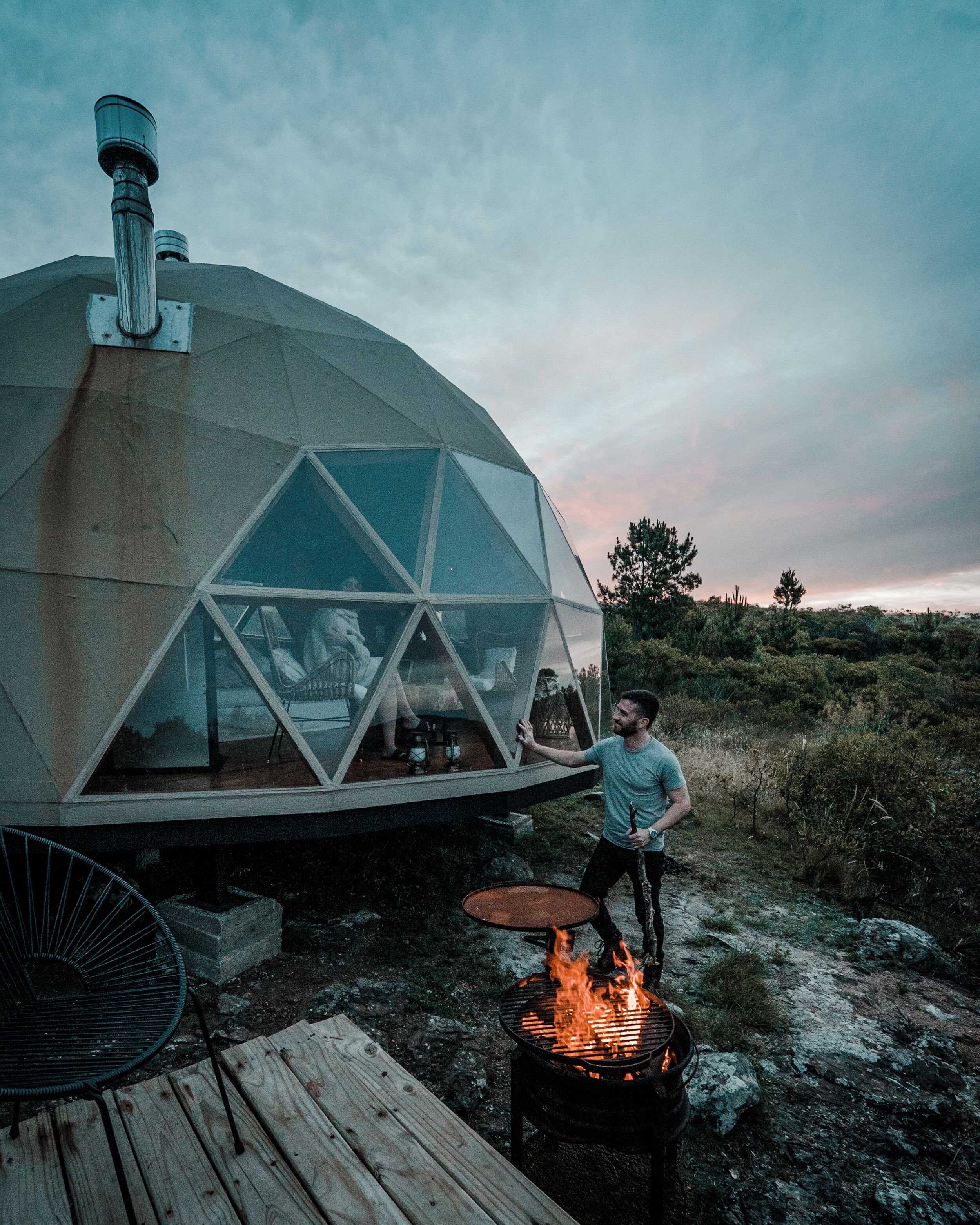 Une structure en forme de dôme géodésique, dotée d’un foyer et d’une terrasse en bois.