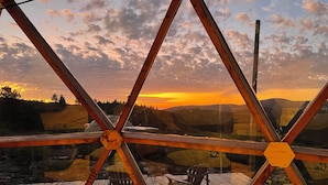 A wooden deck with two chairs and a table, overlooking a scenic landscape with hills and a sunset. - Piedra de las Animas (Nueva Carrara)