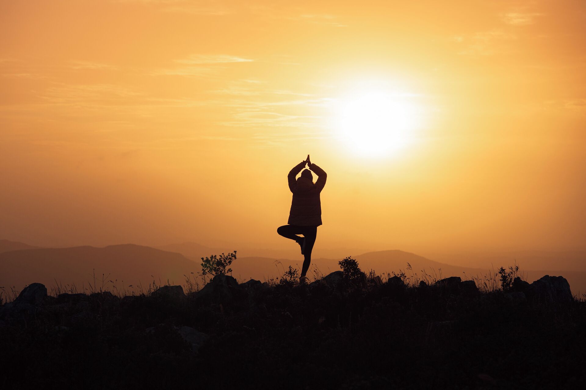 A silhouette of a person performing a yoga pose against a sunset.