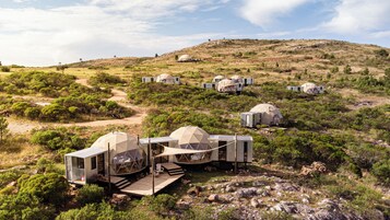 A series of dome-shaped accommodations in a natural landscape with a dirt path leading to a wooden deck.
