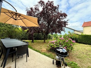 En uteplats med ett bord och stolar, en grill och ett stort träd.