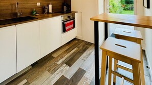 Une cuisine moderne avec des armoires blanches, un plan de travail en bois et un four encastré. Une fenêtre offre une vue sur la verdure à l’extérieur.