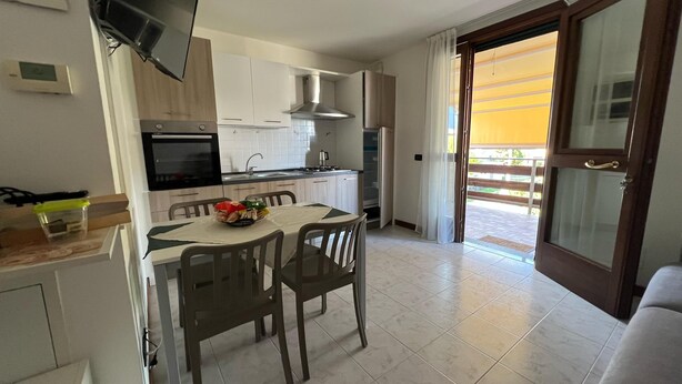 Una cocina compacta con comedor, televisor y puerta corrediza de vidrio a un balcón exterior.