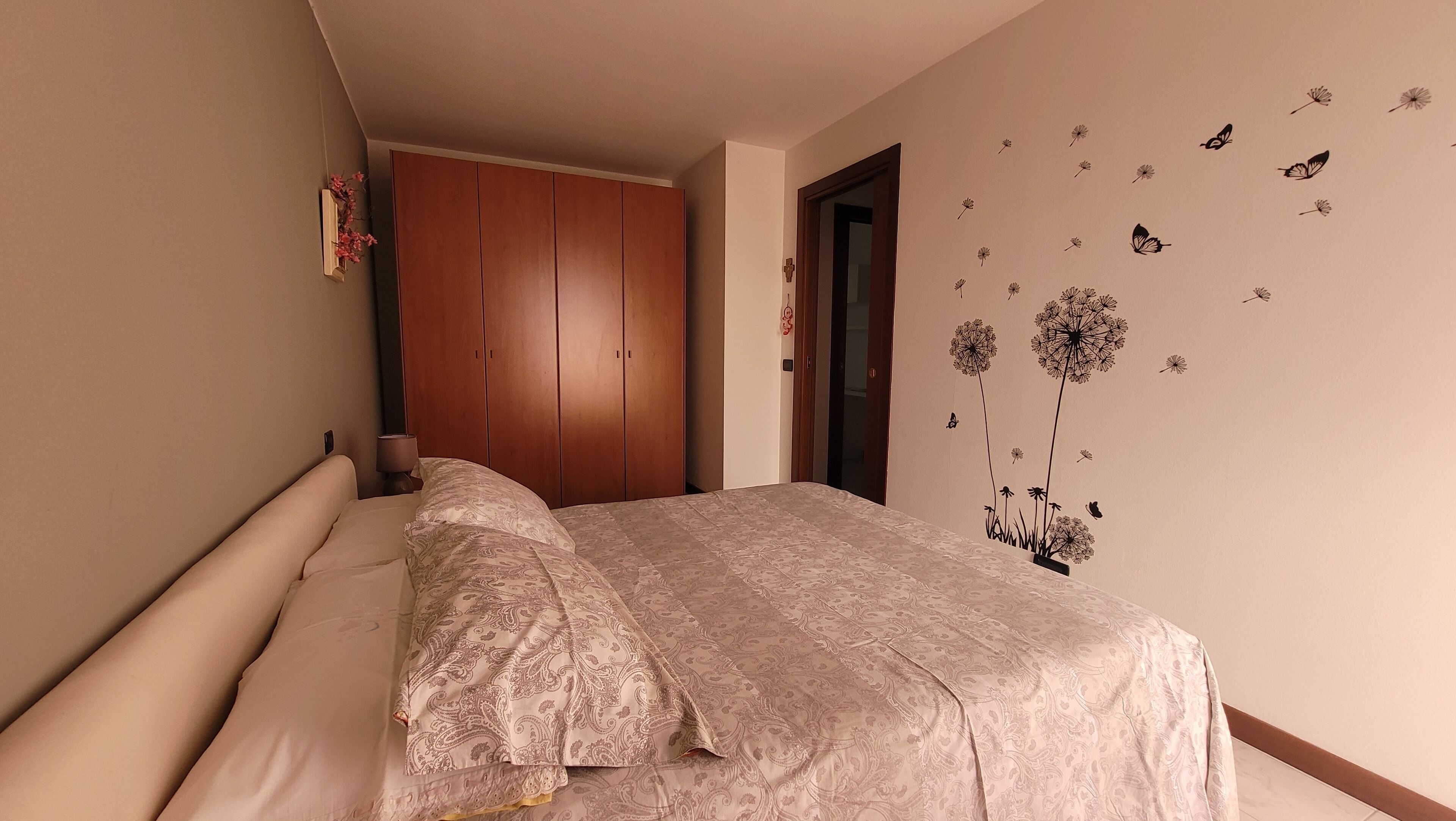 A bedroom with a bed, wooden wardrobe, and a wall decorated with nature-themed decals.