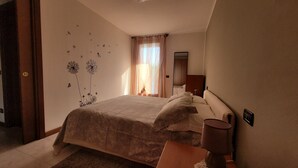 Un dormitorio con una cama grande, una mesita de noche, una lámpara, un espejo y una ventana con cortinas ligeras.