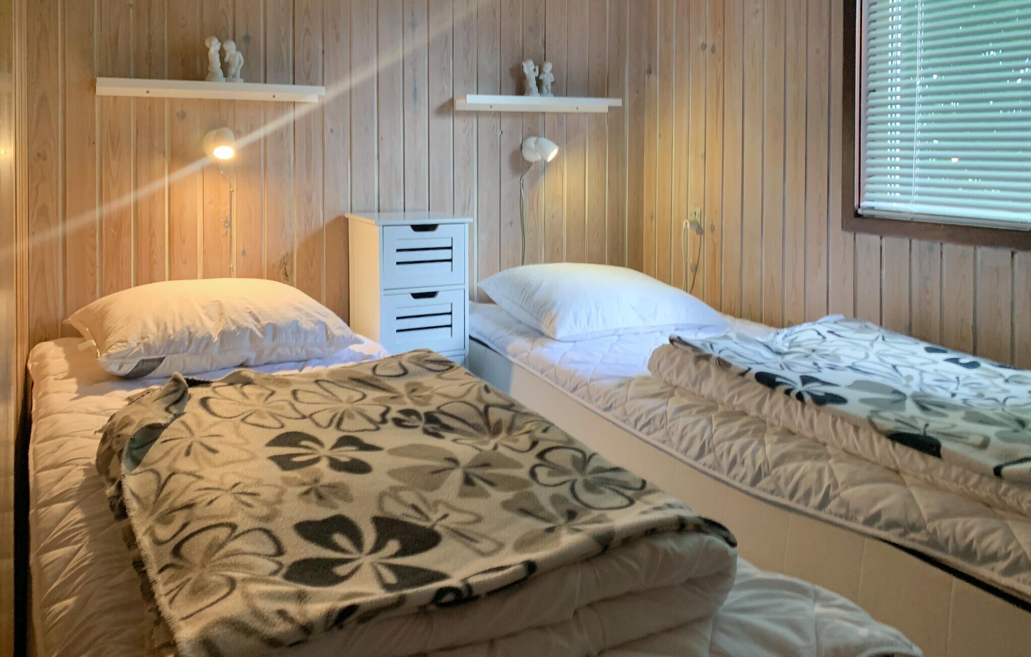 Une chambre avec deux lits, des murs en bois et une fenêtre avec des stores.