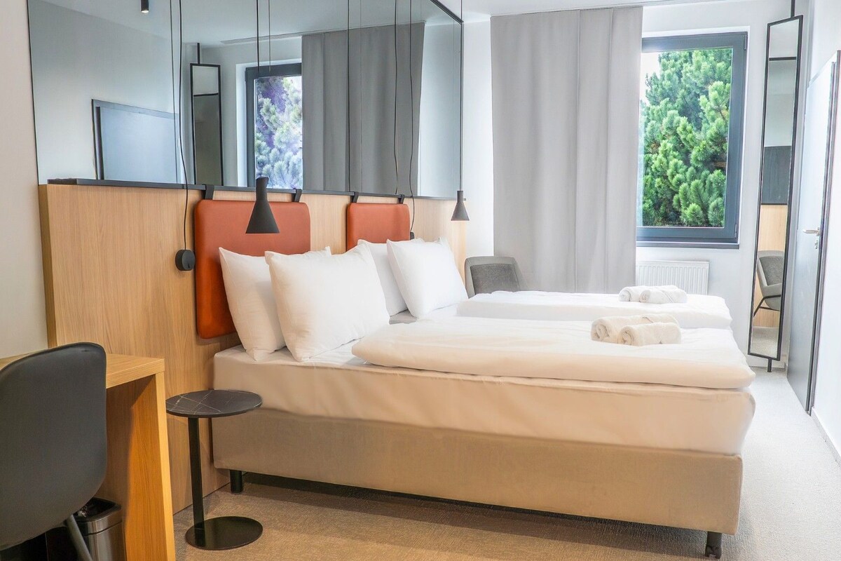 A modern hotel room with a bed, two bedside tables, a desk, and a chair.