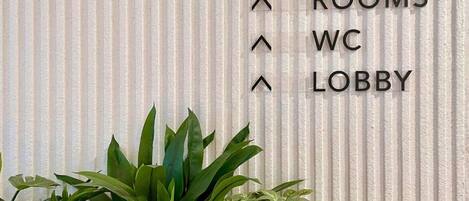 A wall with directional arrows and text indicating 'ROOMS,' 'WC,' and 'LOBBY' locations.