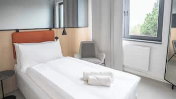 Ein Hotelzimmer mit Bett, Sessel, kleinem Tisch, Fenster mit Blick auf Bäume und Heizkörper.