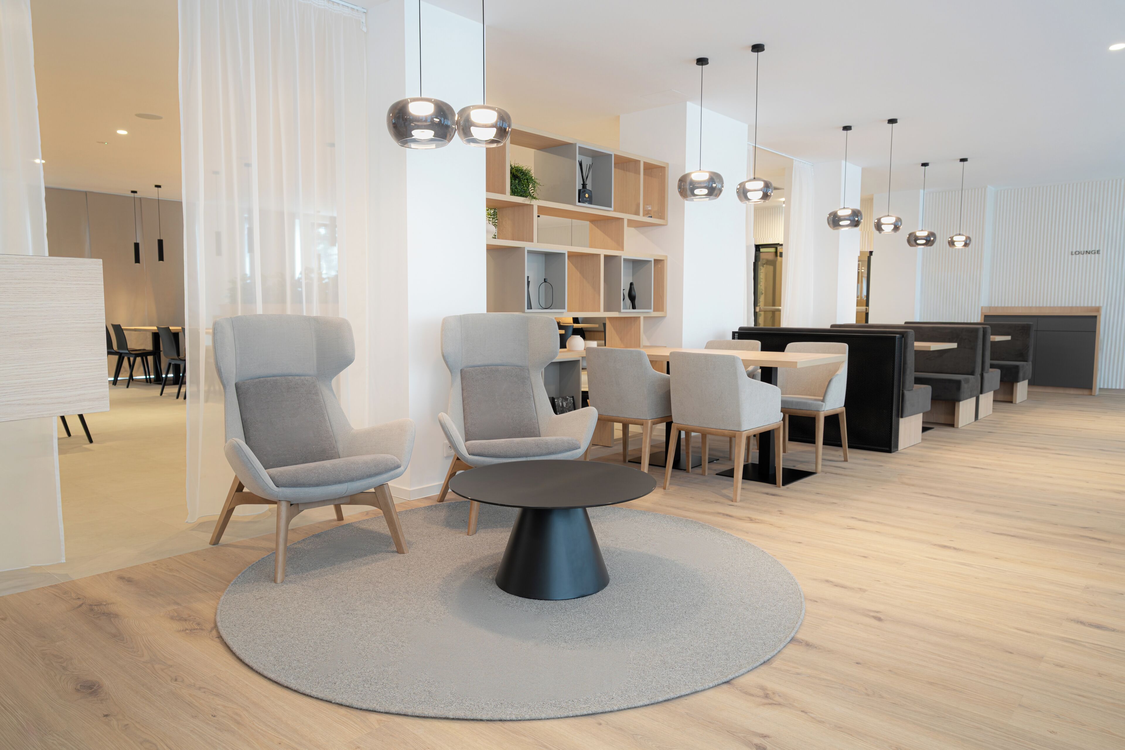 A modern lounge area with round tables, grey upholstered chairs, and pendant lighting.