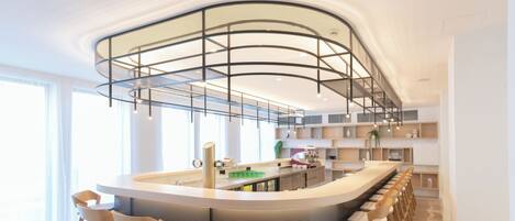 Una cocina moderna con una isla curva, taburetes de bar y un techo alto con un diseño de iluminación único.