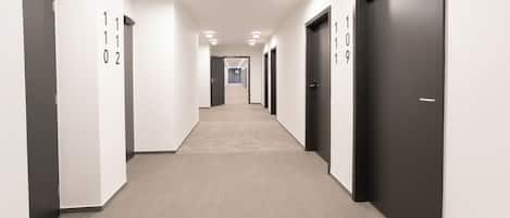A modern hotel corridor with numbered doors, a carpeted floor, and recessed ceiling lights.