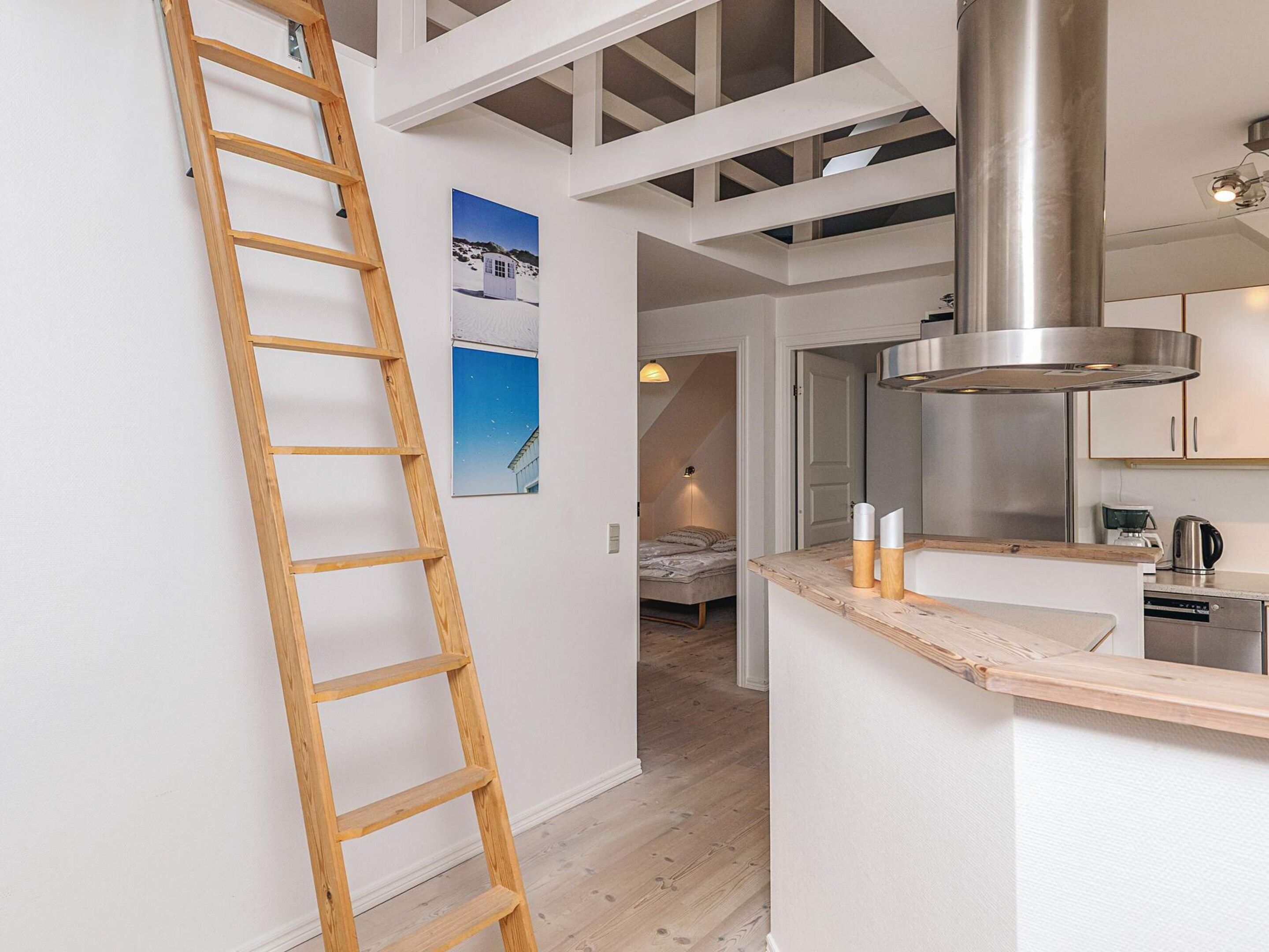 Ein modernes Interieur mit einer Holzleiter, einer Küchenzeile und einem Schlafbereich mit Bett sowie einem an der Wand hängenden Bild.
