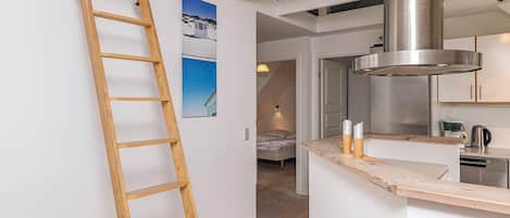 Ein modernes Interieur mit einer Holzleiter, einer Küchenzeile und einem Schlafbereich mit Bett sowie einem an der Wand hängenden Bild.