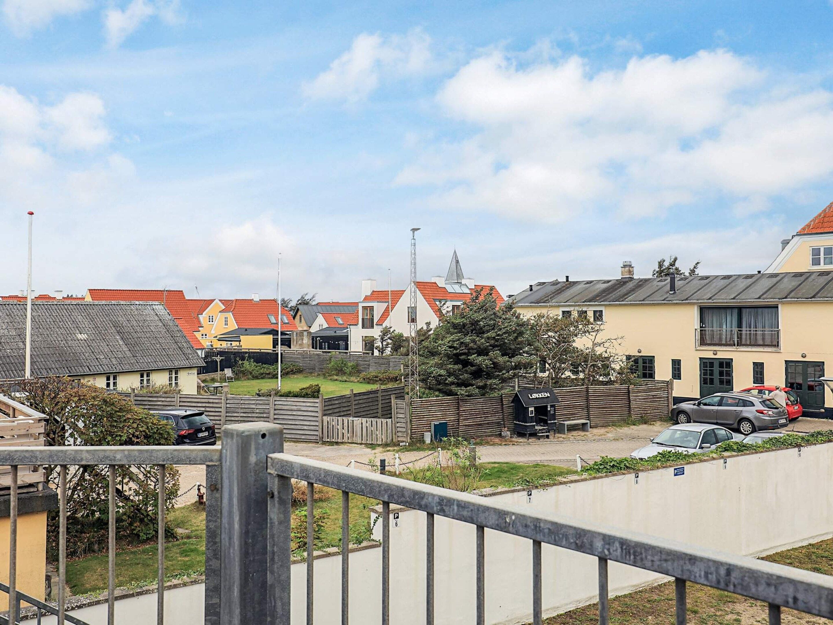 A residential area with houses, a wooden fence, and parked cars.