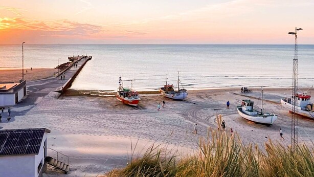 A beach with boats, a pier, and a few people walking. - 5 Star Holiday Home in Lokken (Lokken)