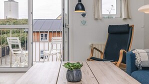 A room with a wooden table, a potted plant, a blue chair, and a view of a building with a silo through a glass door. - 5 Star Holiday Home in Lokken (Lokken)