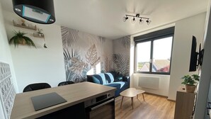 Una cocina moderna con una isla central, una zona de comedor con una mesa pequeña y sillas, un sofá azul y un ventanal con vistas.