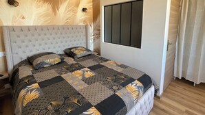 Un dormitorio con un cabecero capitonado, un ventanal con persianas, una cama con colcha estampada y una puerta con cortina.