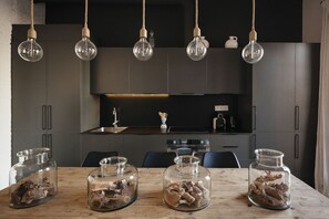 Cozinha moderna com armários escuros, mesa de madeira e luminárias pendentes.