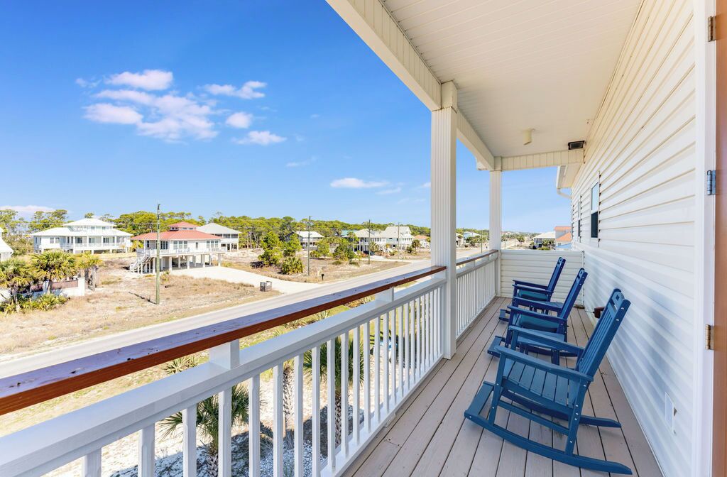 A balcony with a white railing, blue Adirondack chairs, and a view of a residential area with houses and trees.