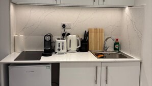 Eine kleine Küche mit weißen Schränken, einem integrierten Kühlschrank, einer Spüle und einer Arbeitsplatte mit Wasserkocher, Toaster und Kaffeemaschine.