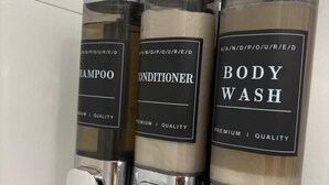 Drei Flaschen Duschgel, Shampoo und Conditioner an einer Wand.