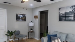 Ein Wohnzimmer mit grauem Sofa, einem kleinen Beistelltisch, einem Topfpflanzen und einem gerahmten Bild an der Wand.
