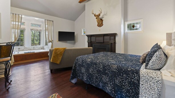 Une chambre à coucher comprenant un lit, une tête de cerf fixée au mur, une cheminée, un téléviseur et une vue sur l’extérieur par une fenêtre.