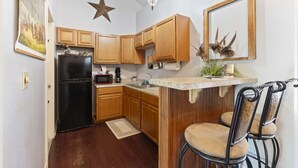 Une cuisine avec des meubles de rangement en bois, un réfrigérateur noir, un four à micro-ondes et un évier. Il y a une décoration en forme d’étoile au plafond et un tableau encadré au mur.