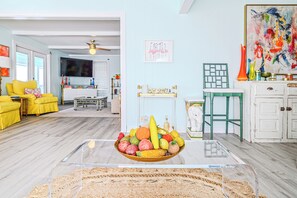 A living room with a glass coffee table, yellow chairs, a TV, and a painting on the wall. - Lose all your worries at Rockport’s most colorful hideaway, Bay Window Retro Retreat! (Rockport)