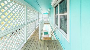 A wooden deck with a white lattice railing, a small set of stairs, and a window with blinds.