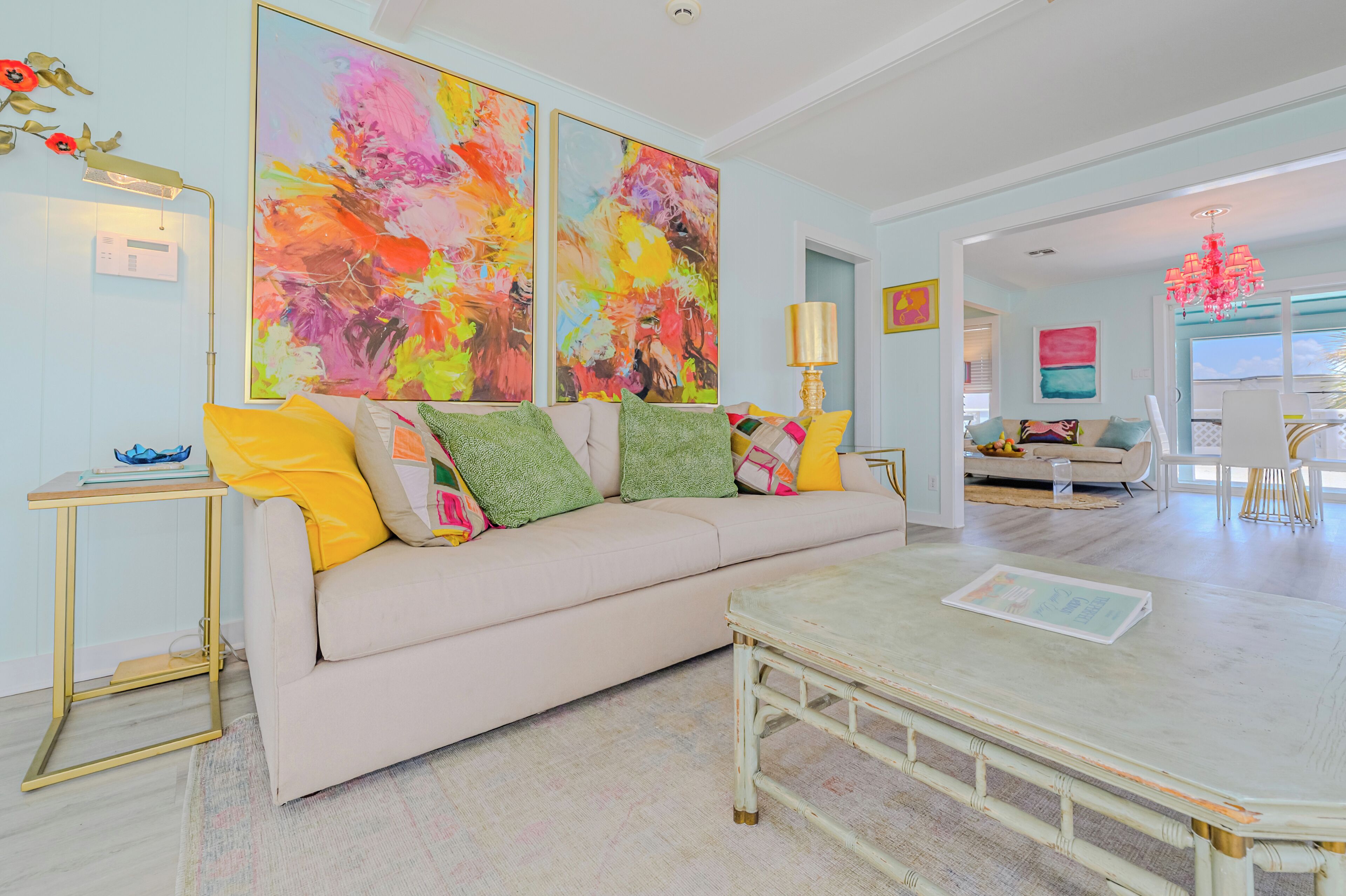 Una sala de estar con un sofá color beige, cojines de colores, una mesa de centro y pinturas abstractas en la pared.