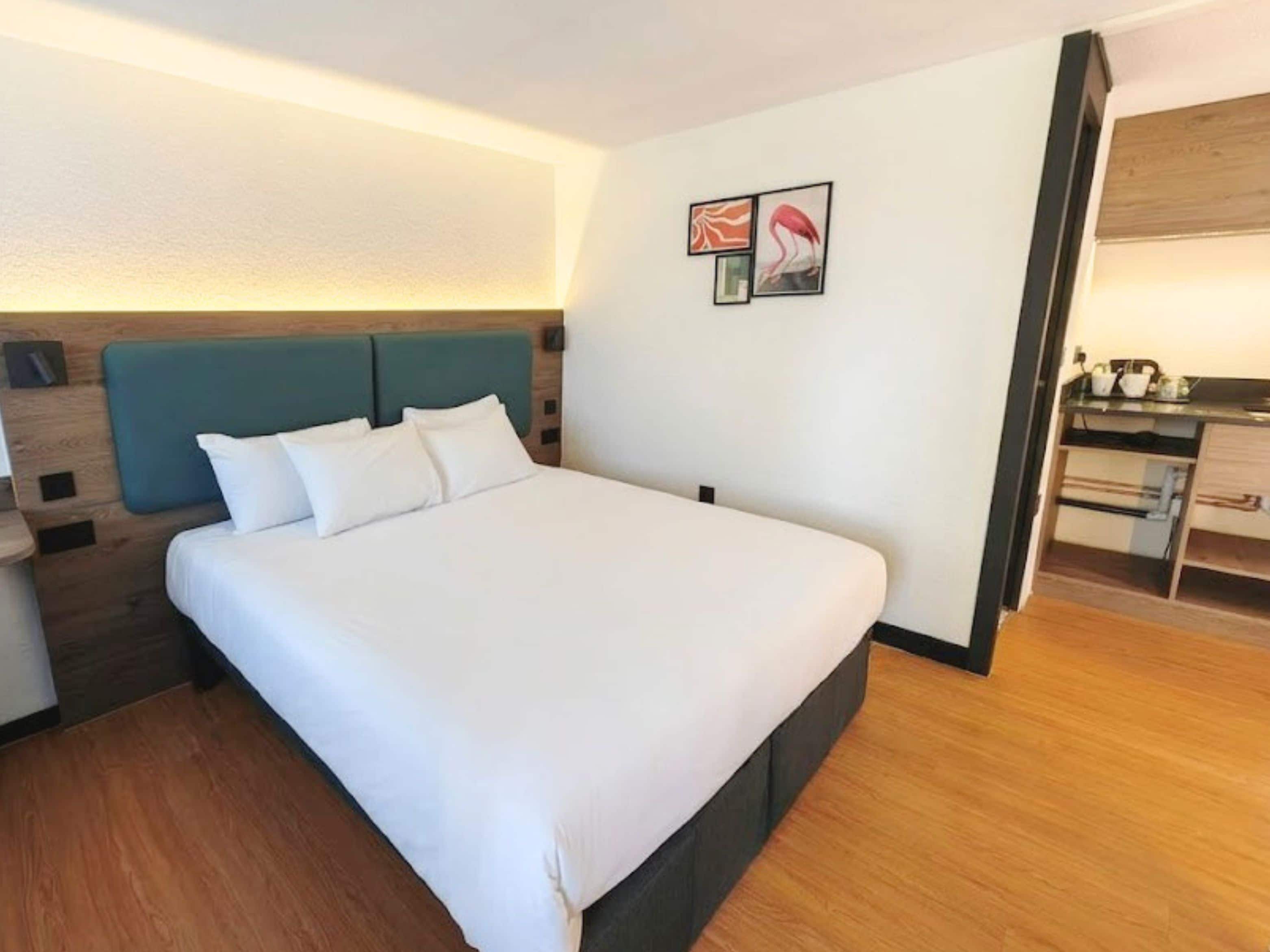 A hotel room with a bed, a nightstand, a desk, and a kitchenette.