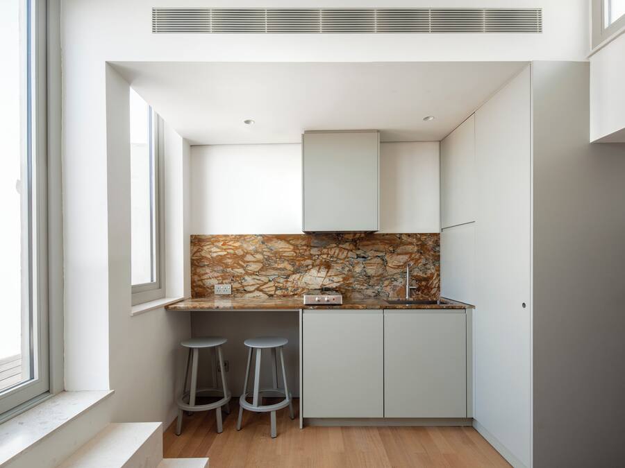 Una cocina compacta con protector contra salpicaduras de piedra, dos taburetes y una ventana.