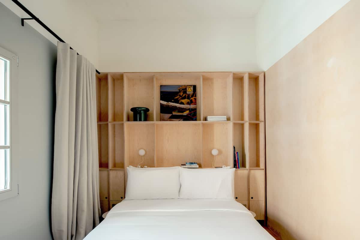 A bedroom with a bed, wooden shelving, and a window with curtains.