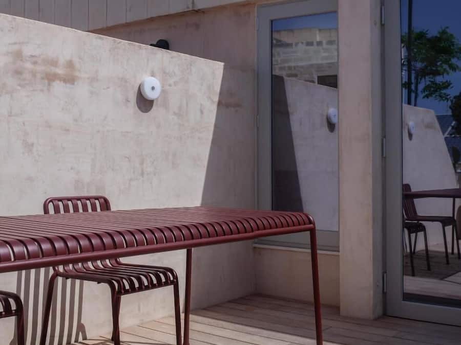 A patio area with a metal table and chairs, a sliding glass door, and a concrete wall.