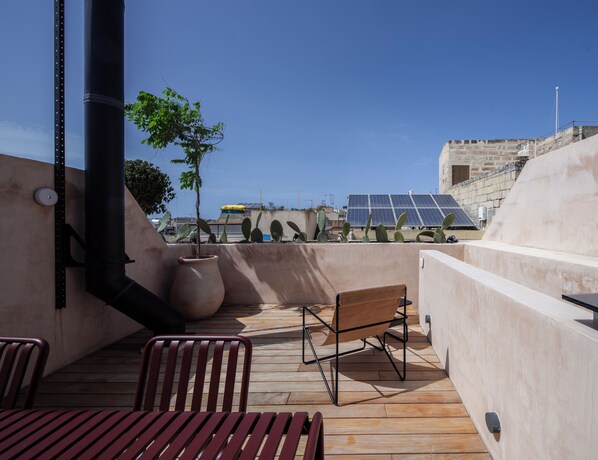 A rooftop terrace with a wooden deck, metal chairs, a potted plant, and solar panels in the background. - Stilla, 6, Triq San Lazzru (Cospicua)