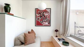 A modern, minimalist living space with a sofa, a small table, and a large window.